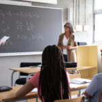 Teen male high school student giving oral class presentation. Teacher listening. Education concept.